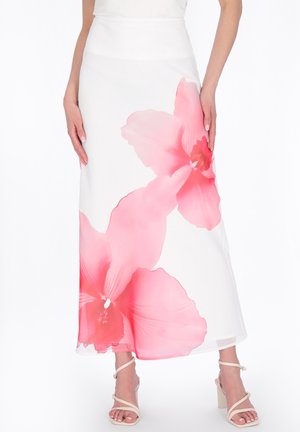 Jupe maxi blanche avec de grandes impressions florales roses douces, portée avec des sandales à talons hauts beiges à lanières.