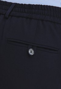 Granatowe spodnie z elastycznym stanem, z zapięciem na guzik i małym detalem w postaci kieszeni z tyłu. Miękki, teksturowany materiał.