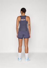 Sporttop in donkergrijs met witte stiksels, racerback ontwerp en uitsnede aan de achterkant. Gecombineerd met bijpassende donkere shorts en sportieve schoenen.