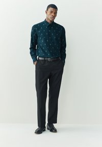 Mørkegrøn skjorte med knapper og lille træmønster, kombineret med sorte bukser og sorte pæne sko. Glat stof og skræddersyet pasform.