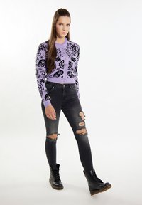 Hellblauer Cardigan mit schwarzem Blumendesign, kombiniert mit zerknitterten schwarzen Skinny Jeans und schwarzen Schnür-Stiefeletten.