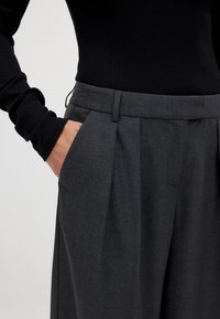 Grijze op maat gemaakte broek met twee voorplooien, riemlussen en zijzakken, gecombineerd met een zwart geribbeld lang mouwtop.