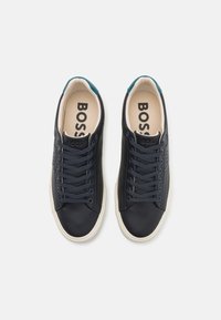 Marineblauwe leren sneakers met een gladde textuur, witte rubberen zool, donkerblauwe veters en een teal accent op de achterkant van de hiel. "BOSS" logo zichtbaar aan de binnenkant.