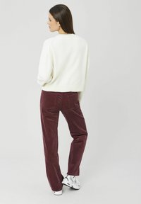 Pull en maille blanche, coupe ample, ourlet côtelé. Pantalon en velours côtelé bordeaux, jambe droite, deux poches arrière. Chaussures de sport blanches avec accents de design.