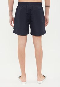 Marinblå badshorts med elastisk midja, kort längd och bakficka. Tyget verkar vara lätt och vattenavvisande.