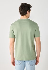 Green cotton t-shirt with a crew neckline and short sleeves, viewed from the back. The fabric appears soft with minimal texture.