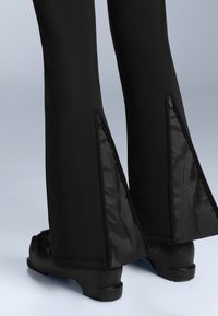 Černé lyžařské kalhoty s bočními zipovými ventily na lemě, vyrobené z hladkého, odolného materiálu. Spodní okraje jsou mírně rozšířené.