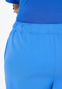 Pantalones cortos de una banda elástica azul, hechos de un material suave y ligero con bolsillos laterales y un ajuste relajado. Sin patrones o detalles notables.