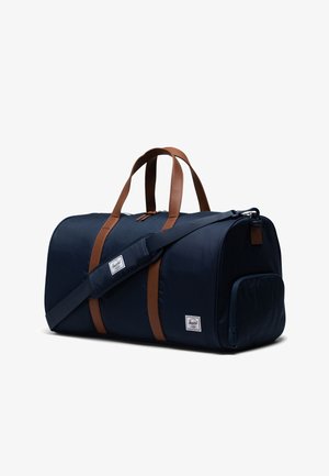 Námornícka modrá športová taška vyrobená z látky s hnedými syntetickými koženými akcentmi. Obsahuje horný zips, dva popruhy na nosenie a nastaviteľný ramenný popruh.