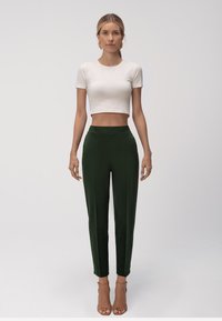 T-shirt bianca cropped abbinata a pantaloni scuri verde scuro a vita alta. I pantaloni presentano un design elegante con una texture liscia e una vestibilità affusolata.