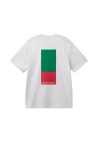 Bílý krátký rukáv tričko s velkým vertikálním zeleným a červeným obdélníkem na zadní straně, červená část zobrazuje slovo "CHROMOTERAPIE" v bílé.