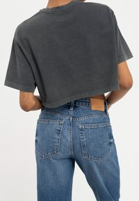 Grå cropped t-shirt med korte ærmer, parret med højtaljede blå denim jeans med en tan læderpatch og baglommer.