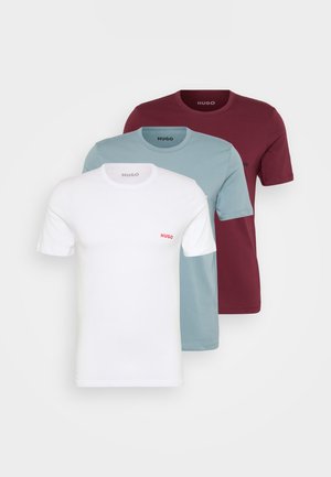 Drie crewneck T-shirts in wit, teal en bordeauxrood, met korte mouwen en een klein rood logo op de linkerborst.