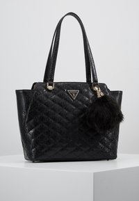 Sac fourre-tout noir matelassé avec motif logo, texture lisse, garnitures dorées, double poignée, et un pompon en fourrure noire amovible.