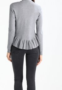 Maglione grigio lavorato a maglia con orlo a peplum a coste, collo rotondo e maniche lunghe. Indossato con jeans skinny neri. Vista posteriore mostrata.
