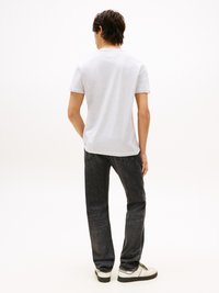 Grau kurzärmliges T-Shirt, das von einer Person getragen wird, die dunkle Jeans und weiße Sneaker trägt, mit einem einfachen Design und rundem Halsausschnitt.