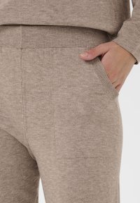Pantaloni tricotati bej cu o textură moale, având buzunare laterale și un elastic ribat pentru o fixare sigură.