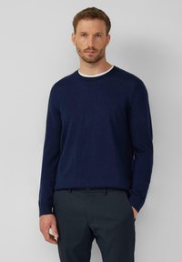 Granatowy sweter z długim rękawem, wykonany z gładkiej dzianiny, z białą ribbowaną okrągłą ławką i luźnym krojem. W połączeniu z ciemnymi spodniami.