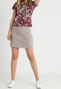 Röd och vit blommönstrad kortärmad topp i kombination med en ljusbeige kjol som går ovanför knäet och vita sneakers. Släta tyger.