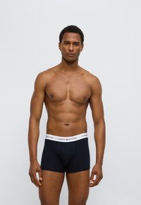 Μαύρα βαμβακερά εσώρουχα μποξέρ με λευκή ελαστική ζώνη μέσης που φέρει το λογότυπο "TOMMY HILFIGER" σε κόκκινο και μπλε. Λείο ύφασμα και εφαρμοστή γραμμή.