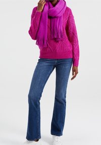 Světle růžový pletený svetr s diamantovými vzory, doplněný shodným šátkem. Úzké modré džíny a bílé tenisky dokončují celkový vzhled.