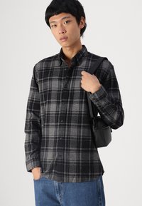 Μαύρο και γκρι καρό πουκάμισο φλις με μακριά μανίκια και γιακά που κουμπώνει, συνδυασμένο με μπλε τζιν παντελόνι και μια μικρή μαύρη τσάντα.