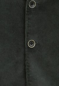 Ciemnozielony materiał kordurowy ma pionową teksturę prążków, dwa okrągłe metalowe guziki oraz listwę guzikową na środku.