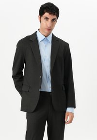 Dark gray tailored blazer with structured shoulders, single-button closure, and two front pockets, paired with a light blue dress shirt.