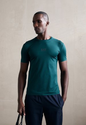 Short-sleeve athletic shirt in dark green, smooth fabric with a fitted design. Features a small EA7 logo in the center front.