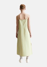 Hellgrünes, ärmelloses Maxikleid mit geradem Design, verstellbaren Trägern und seitlichen Schlitzen, kombiniert mit weißen Sneakers und Knöchelsocken.