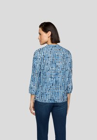 Blau gemusterte Bluse mit dreiviertel Ärmeln, mit einem kreisförmigen Design in verschiedenen Blautönen. Rückansicht, leichtes Gewebe.