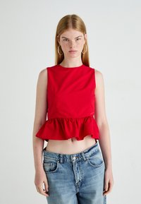 Rød ermeløs topp med peplum-søm, laget av glatt stoff. Kombinert med høyhælte, lyseblå, lett slitte jeans.