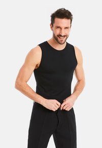 Black sleeveless tank top made of stretchy fabric, features a round neckline and a fitted design, paired with black trousers.