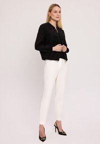 Czarna kurtka bomberka z teksturowanym wzorem, dopasowana w talii, z zapięciem na zamek, noszona na czarnym topie i białych spodniach; w połączeniu z czarnymi szpilkami.