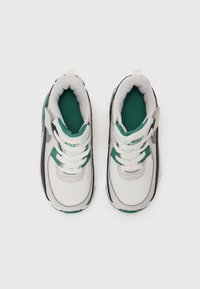 Baskets de sport blanches avec des accents verts, doublure en mesh et semelle en caoutchouc. Caractéristiques d'une sangle en velcro et de lacets pour un ajustement sécurisé.