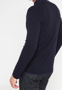 Suéter de punto de manga larga en color navy con un diseño de punto texturizado y un cuello en contraste. Corte ajustado con puños y dobladillo acanalados.