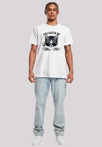 Weißes Baumwoll-T-Shirt mit einem schwarz-weißen Katzendesign, das eine Sonnenbrille trägt, sowie dem Text "YOU GOTTA BE Kitten Me!" in fetter Schrift. Bequeme Passform.