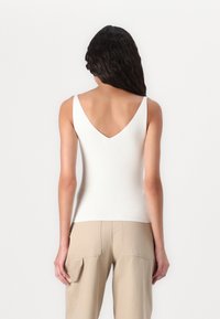Witte geribde tanktop met een diepe V-rug en smalle bandjes, met een aansluitend ontwerp dat zich vormt naar het lichaam, gedragen met beige cargobroeken.