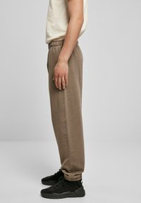 Brune avsmalnede joggebukser med elastisk livlinning og ankelmanchetter, laget av myk stoff, sammen med svarte treningssko.