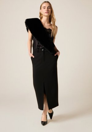 Black satin camisole with lace trim paired with a black high-waisted pencil skirt featuring a front slit. Faux fur shawl draped over one shoulder.