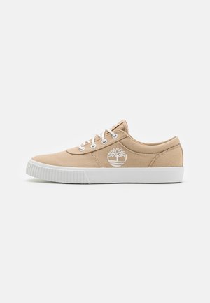 Beige canvas sneaker met een witte rubberen zool, met witte oogjes en veters, en een wit logo-ontwerp aan de buitenzijde.