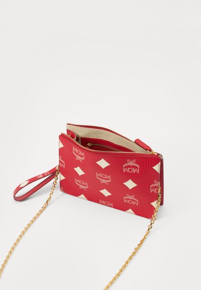 Red textured handbag with cream diamond pattern, gold accents, and chain strap. Features a zip closure and wristlet for carrying convenience.
