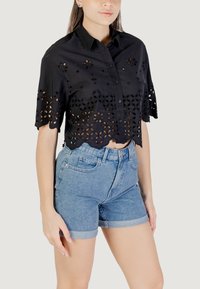 Blusa cropped nera con intagli floreali intricati e orlo scallop, abbinata a pantaloni corti in denim a vita alta con risvolti.