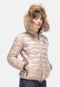 Giacca puffer beige con design trapuntato, cappuccio foderato in pelliccia, chiusura con zip e tasche laterali. La texture è liscia con una finitura lucida.