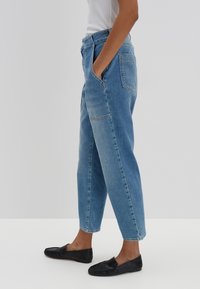 Jeans in denim azzurro chiaro con una vestibilità ampia, vita alta, tasche laterali e cuciture a contrasto. Abbinati a scarpe nere flat slip-on.