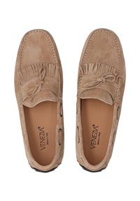 Beige Wildleder-Mokassinschuhe mit Fransen, Schleifenakzent und kontrastierendem Nähen. Schwarze Gummisohle mit dekorativer Schnürung.