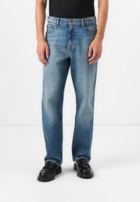 Blauwe spijkerbroek met een relaxte pasvorm, voorzien van een knoopsluiting, vijf zakken en lichte vervaging. Gecombineerd met zwarte instappers.