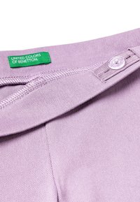 Liliowa odzież o gładkiej teksturze, z zapięciem na guziki i zieloną metką z napisem "United Colors of Benetton."