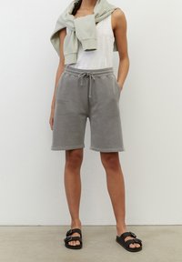 Shorts gris en mélange de coton avec une taille élastique et un cordon de serrage, poches latérales et coupe décontractée, assortis à un débardeur blanc et un pull vert clair.