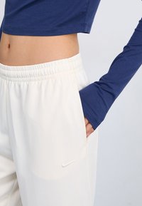 Tengeri kék hosszú ujjú felső, krémszínű, csíkozott jogger nadrággal párosítva, rugalmas derékpánttal; Nike logó az oldalon.